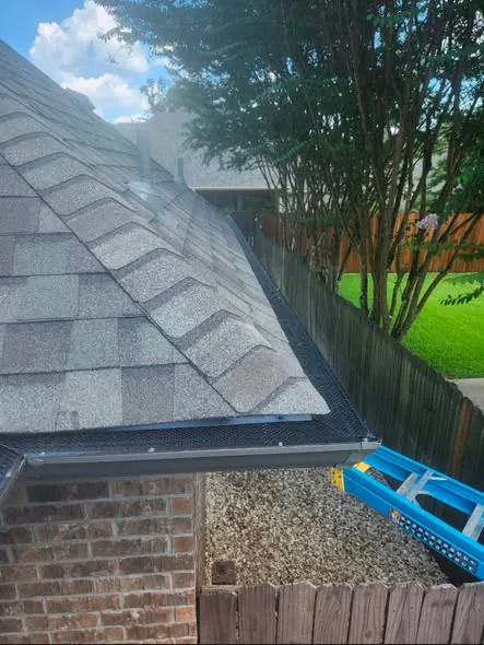 Mesh gutter guard following a corner of a shingle roof beside a brick wall