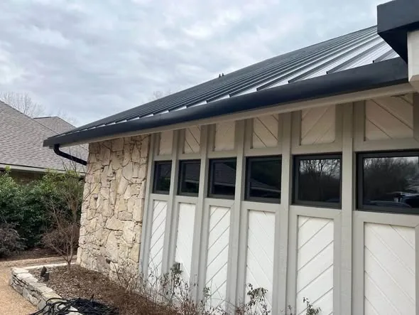 Black gutter beneath a metal roof above white paneled doors and stone walls