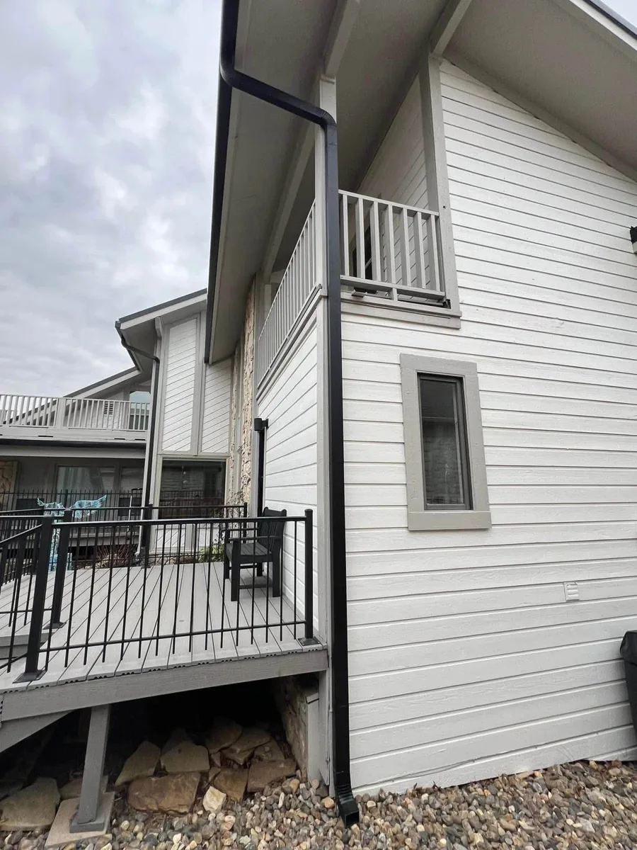 Dark downspout running beside white siding beneath a roof overhang